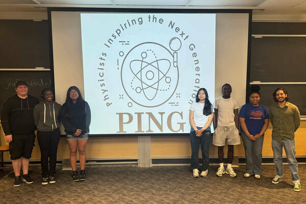 Graduate student Fabio Rivero and five local high school students stand in front of a projector that says  Physicists Inspiring the Next Generation.