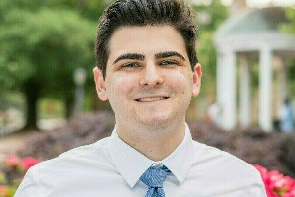 Portrait of Noah Cabanas in a white shirt and a blue tie.